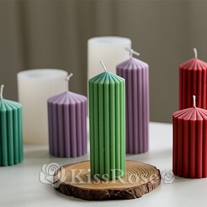 May include: Assortment of six pillar candles in various colors, including green, purple, red, and white. The candles have a ribbed design and are arranged on a wooden slice.