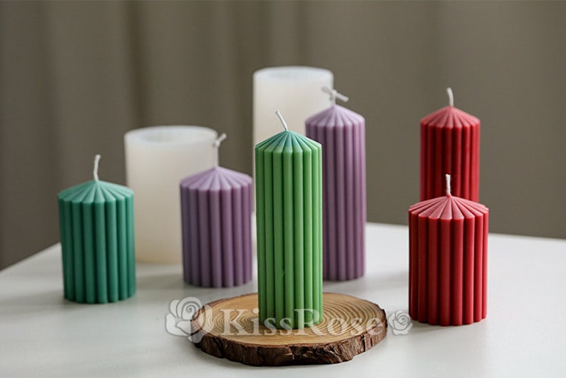 May include: Assortment of six pillar candles in various colors, including green, purple, red, and white. The candles have a ribbed design and are arranged on a wooden slice.
