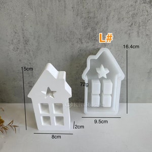 Może przedstawiać: Biała plastikowa forma do robienia małej świeczki w kształcie domu. Forma ma 15 cm wysokości, 8 cm szerokości i 12 cm głębokości. Ma wycięcie w kształcie gwiazdy na g&oacute;rze i wz&oacute;r okna z przodu. Forma jest oznaczona "L#" i waży 72 gramy.