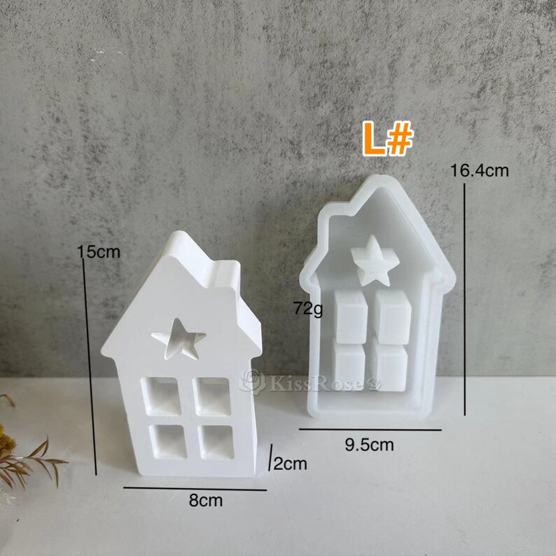 Może przedstawiać: Biała plastikowa forma do robienia małej świeczki w kształcie domu. Forma ma 15 cm wysokości, 8 cm szerokości i 12 cm głębokości. Ma wycięcie w kształcie gwiazdy na g&oacute;rze i wz&oacute;r okna z przodu. Forma jest oznaczona "L#" i waży 72 gramy.