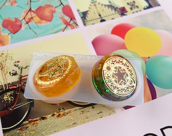 May include: Two resin pendants in a silicone mold. One is amber-colored with a gold star design, the other is green and gold with a star and circle design. The mold is on a background with colorful images.