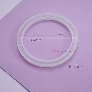 May include: White silicone ring mold with two different sized circles. The outer circle measures 112 mm and the inner circle measures 95 mm. The mold is 1.1 cm high.