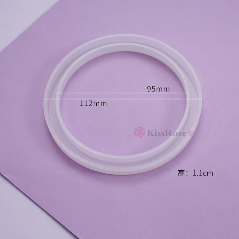 May include: White silicone ring mold with two different sized circles. The outer circle measures 112 mm and the inner circle measures 95 mm. The mold is 1.1 cm high.