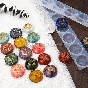 May include: A set of 12 chakra stones with gold symbols on a white fabric background. The stones are arranged in a circle and are surrounded by a clear silicone mold with the same chakra symbols.