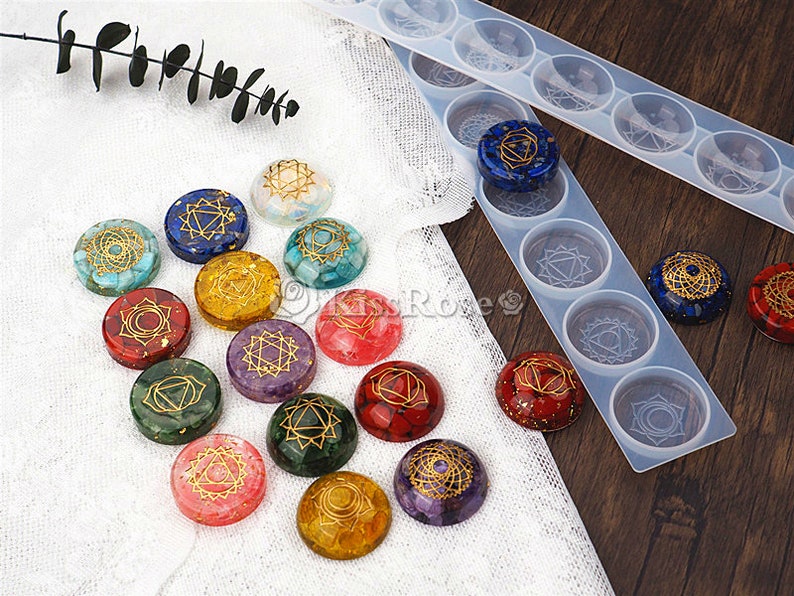 May include: A set of 12 chakra stones with gold symbols on a white fabric background. The stones are arranged in a circle and are surrounded by a clear silicone mold with the same chakra symbols.