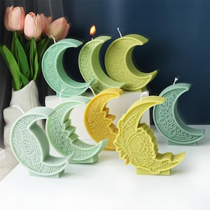May include: A set of seven green and yellow crescent moon shaped candles with intricate designs. The candles are made of wax and have a traditional look.