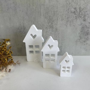 May include: Three white wooden houses with heart cutouts and window details. The houses are arranged in descending size order.