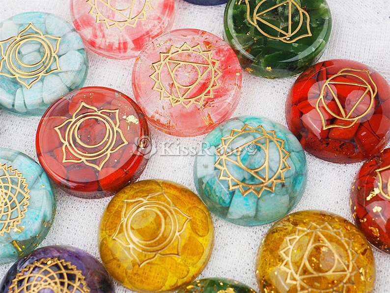 May include: Seven round, polished stones with gold geometric designs. Each stone is a different color, including red, green, blue, white, and yellow.