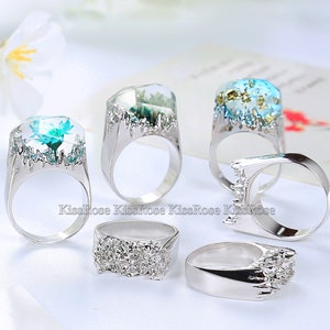 May include: Five silver rings with different designs. Each ring features a clear resin setting with a pressed flower or other botanical element. The rings are all different sizes and styles.
