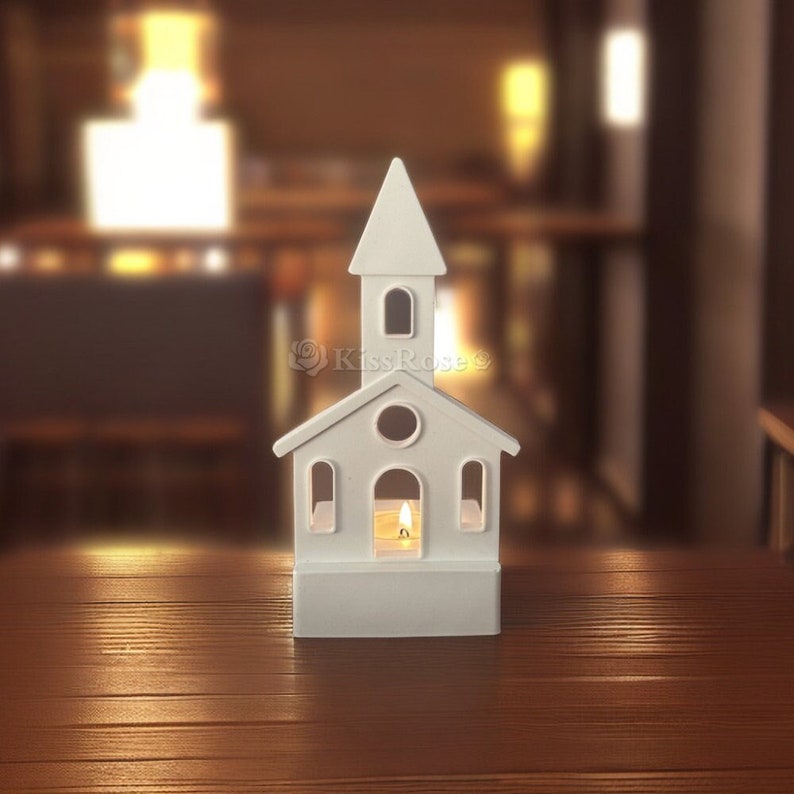 May include: White ceramic church-shaped candle holder with a small candle inside. The candle holder is on a wooden surface.