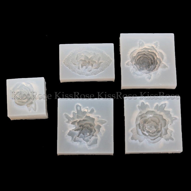 May include: Five silicone molds for making various flower shapes. The molds are white and have a smooth surface. The flower shapes include a single rose, a rose with leaves, and three different peony shapes.