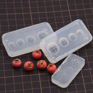 Puede incluir: Tres moldes de silicona transparentes para hacer peque&ntilde;as formas de fruta roja. Los moldes son rectangulares y tienen diferentes dise&ntilde;os. Hay cinco peque&ntilde;as formas de fruta roja al lado de los moldes.