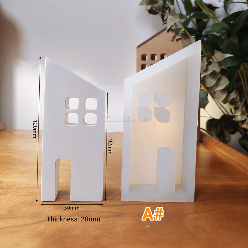 May include: White silicone mould shaped like a small house with a door and windows. The mould is 120mm tall, 92mm wide, and 50mm deep. The mould is 20mm thick. The mould is labelled "A#"