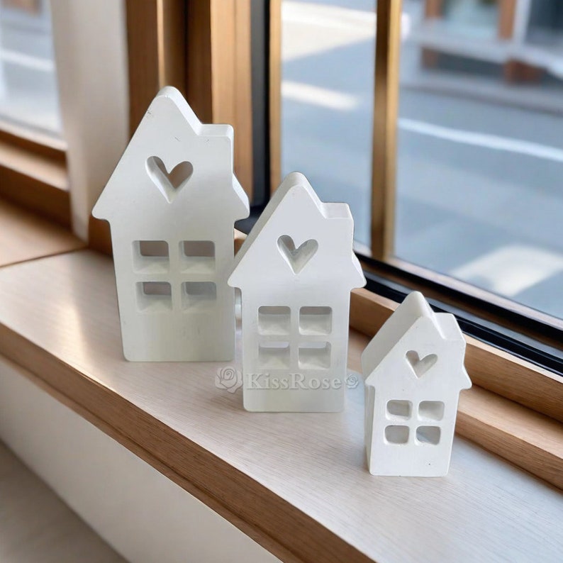 May include: Three white wooden houses with heart cutouts and window details. The houses are arranged in a row from largest to smallest.
