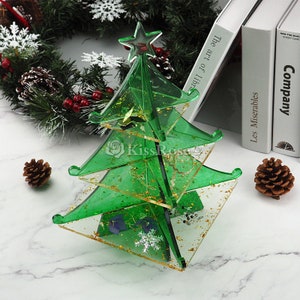 Könnte beinhalten: Ein grüner gläserner Weihnachtsbaumschmuck mit goldenen Glitzer und einem Stern oben. Der Schmuck befindet sich auf einer weißen Marmorfläche.
