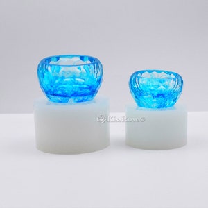 May include: Two clear blue resin bowls with a textured, geometric design. The bowls are sitting on white circular bases.