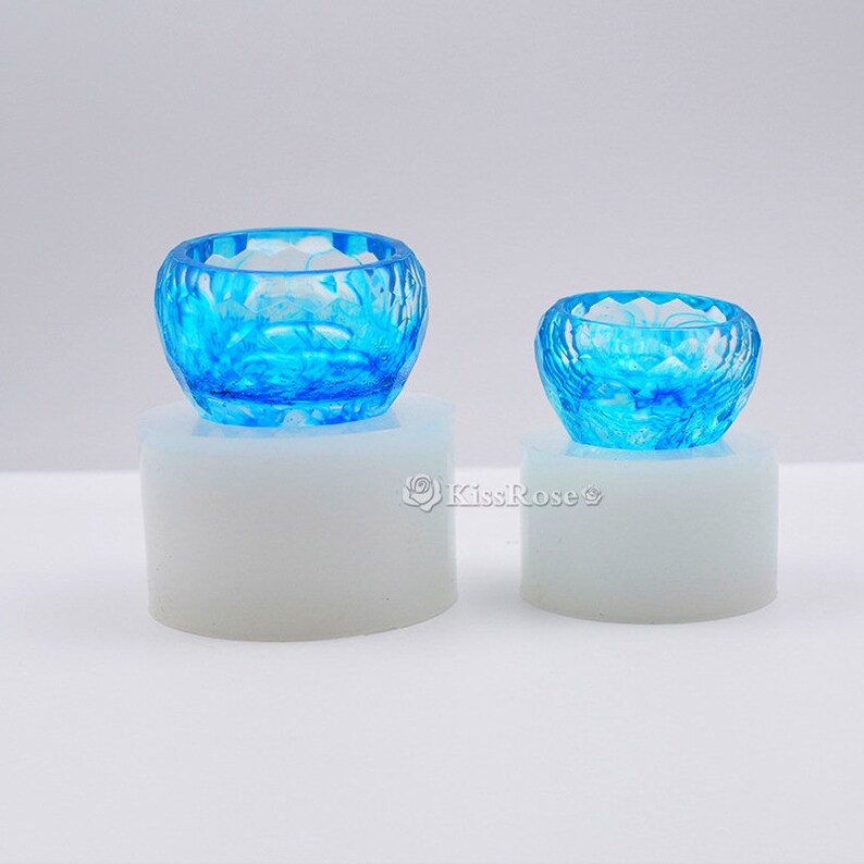 May include: Two clear blue resin bowls with a textured, geometric design. The bowls are sitting on white circular bases.