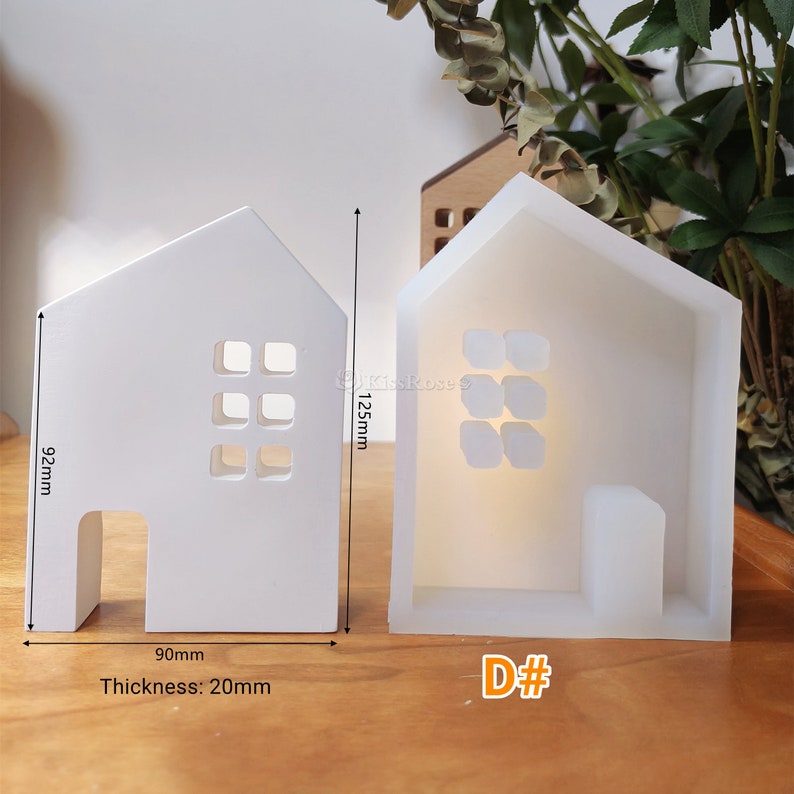May include: White silicone mould shaped like a house with a door and windows. The mould is 12.5 cm tall, 9.2 cm wide, and 2 cm thick. The mould is labelled "D#"