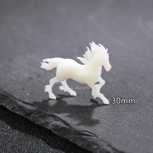 Op de afbeelding: Witte resin paardenbeeldje, 30 mm groot. Het paard rent met zijn manen in de wind.