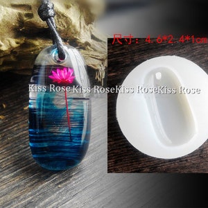 May include: A clear resin pendant with a pink flower inside, hanging from a black cord. The pendant is 4.6 inches by 2.4 inches by 1 inch. The pendant is next to a white silicone mold of the pendant.
