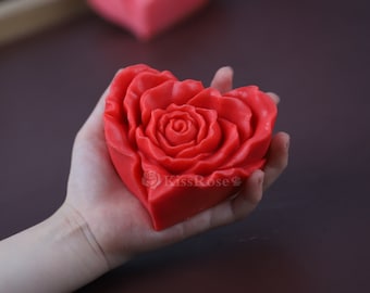 May include: A red heart-shaped soap with a rose design. The soap is in the palm of a hand.