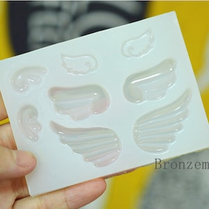 Könnte beinhalten: Weiße Silikonform mit sieben verschiedenen Engelsflügelformen. Die Form ist aus flexiblem Silikon und für die Herstellung von Kunsthandwerk aus Harz konzipiert.