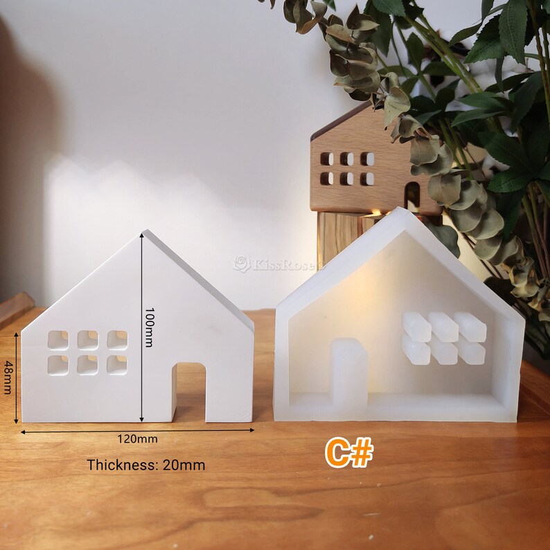 May include: White silicone mould shaped like a house with a window and door opening. The mould is 120mm wide, 100mm tall, and 20mm thick. The mould is on a wooden surface.