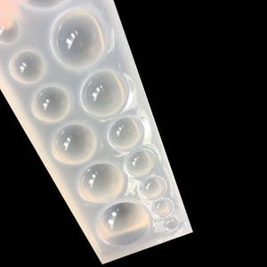 K&ouml;nnte beinhalten: Eine transparente Silikonform mit mehreren runden Vertiefungen in verschiedenen Gr&ouml;&szlig;en. Die Form ist zum Erstellen von Cabochons aus Harz oder Polymer Clay gedacht.