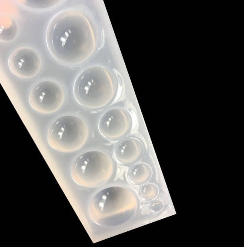 K&ouml;nnte beinhalten: Eine transparente Silikonform mit mehreren runden Vertiefungen in verschiedenen Gr&ouml;&szlig;en. Die Form ist zum Erstellen von Cabochons aus Harz oder Polymer Clay gedacht.