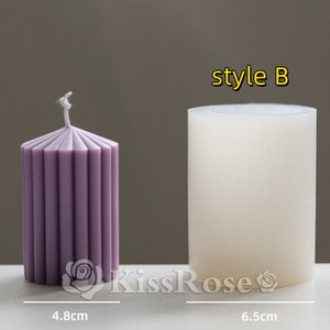 May include: Two pillar candles, one is white and the other is purple with vertical lines. The white candle is labeled "style B". The candles are 8.5 cm tall and 6.5 cm wide.