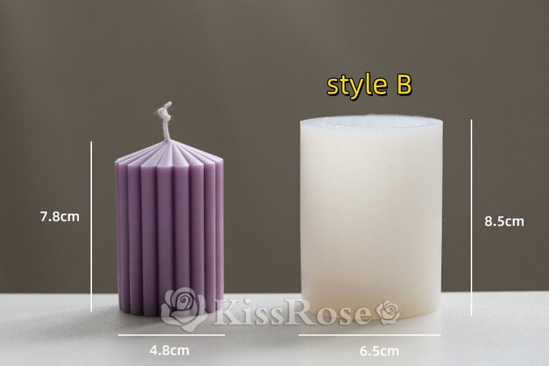 May include: Two pillar candles, one is white and the other is purple with vertical lines. The white candle is labeled "style B". The candles are 8.5 cm tall and 6.5 cm wide.