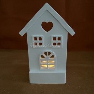 May include: White wooden house shaped candle holder with a heart cutout and two windows. The holder has a space for a tea light candle in the bottom.