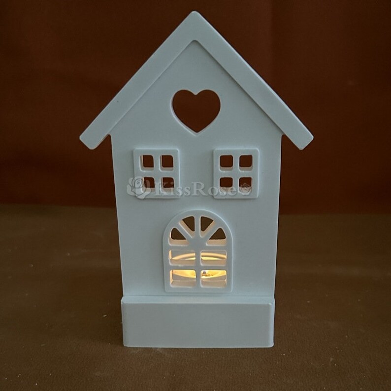 May include: White wooden house shaped candle holder with a heart cutout and two windows. The holder has a space for a tea light candle in the bottom.