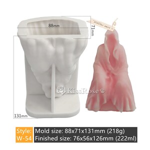 May include: White silicone mold for making a candle in the shape of a hooded figure. The mold is 88mm wide, 71mm deep, and 131mm tall. A finished candle is shown next to the mold. The candle is pink and has a hooded figure shape. The candle is 76mm wide, 56mm deep, and 126mm tall.