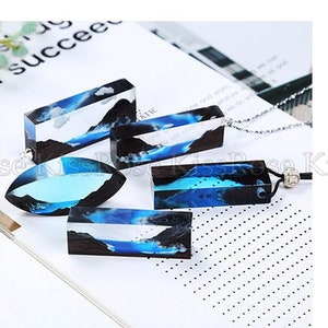 May include: Four resin pendants with blue and black abstract designs. The pendants are rectangular and oval shaped. The pendants are on a white surface.