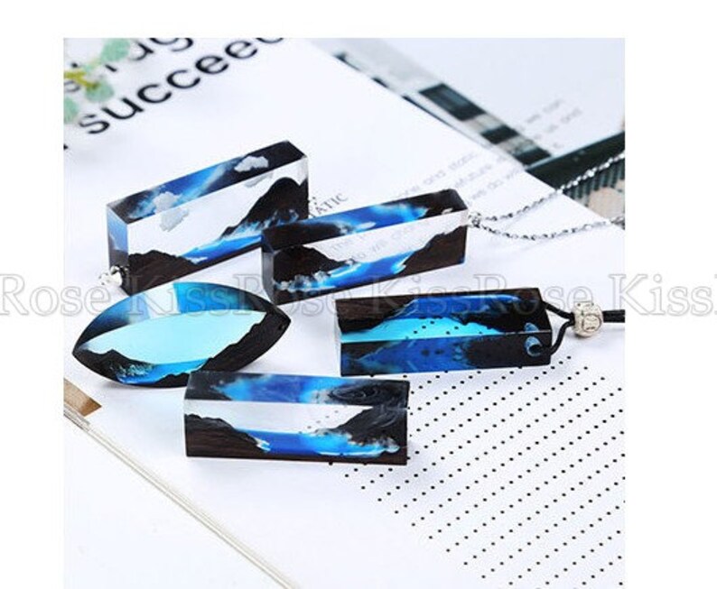 May include: Four resin pendants with blue and black abstract designs. The pendants are rectangular and oval shaped. The pendants are on a white surface.