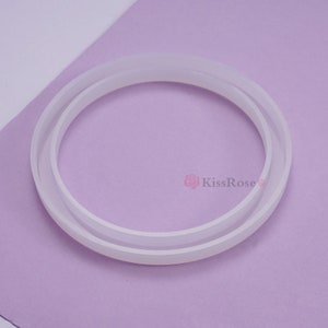 May include: A white silicone ring mold for crafting. The mold is made of two pieces that fit together to create a round shape.