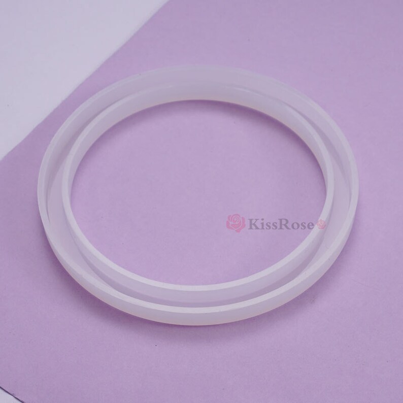 May include: A white silicone ring mold for crafting. The mold is made of two pieces that fit together to create a round shape.