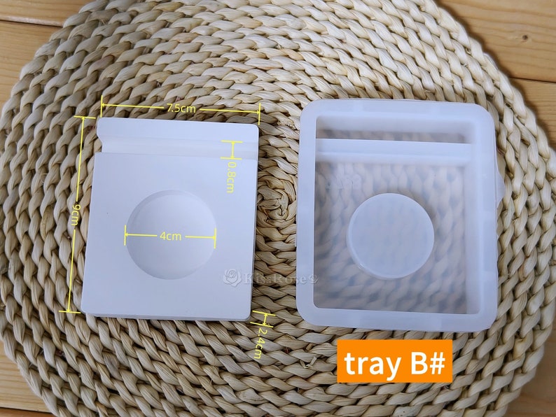 May include: Two white silicone molds for resin casting. The mold on the left is 7.5 cm wide, 9 cm tall, and 10.8 cm deep. The mold on the right is 24 cm tall. The mold on the left has a circular indentation that is 4 cm in diameter. The mold on the right has a rectangular indentation and a circular indentation. The text "tray B#" is printed on the bottom right corner of the image.