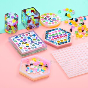 Pode incluir: Conjunto de  tapetes de mosaico de azulejos coloridos, uma bandeja hexagonal, uma bandeja quadrada, uma bandeja redonda e dois pequenos recipientes de vidro. Os azulejos são dispostos em uma variedade de padrões e cores, incluindo vermelho, azul, verde, amarelo e roxo. Há também uma forma de silicone transparente com um padrão de grade.