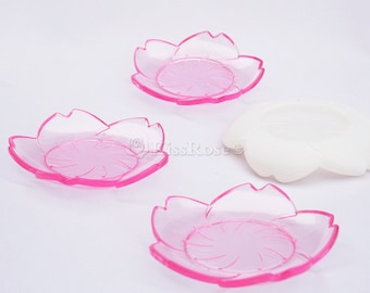May include: Three pink plastic flower-shaped plates with a swirl design in the center. The plates are on a white surface.