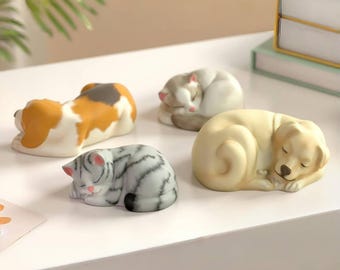 May include: A collection of four sleeping animal figurines: a beagle, two cats, and a golden retriever. The beagle is white, brown, and tan. One cat is gray and white striped, and the other is white and gray. The golden retriever is light yellow.