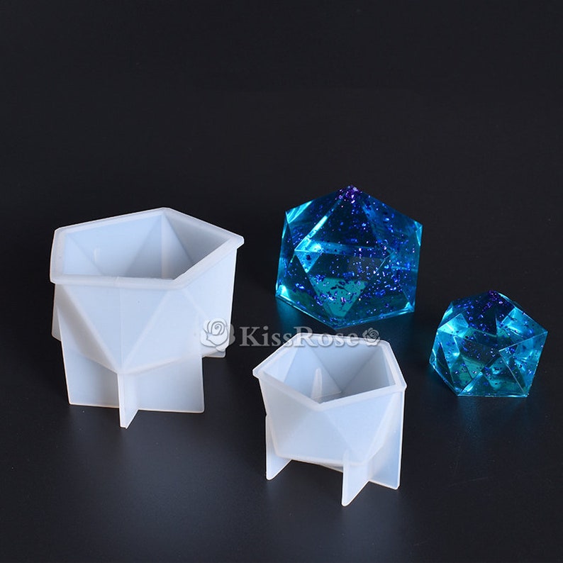 K&ouml;nnte beinhalten: Zwei wei&szlig;e Silikonformen zum Herstellen von geometrischen Harzformen. Die Formen haben die Form einer sechseckigen Pyramide mit quadratischer Basis. Die Formen werden mit zwei fertigen Harzst&uuml;cken gezeigt, einem gro&szlig;en und einem kleinen, beide mit einer blauen und violetten Glitzer-Oberfl&auml;che.