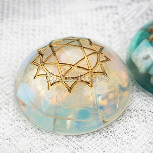 May include: Two round, clear resin ornaments with gold geometric designs. One ornament is filled with iridescent white and blue pieces, the other is filled with blue and green pieces.