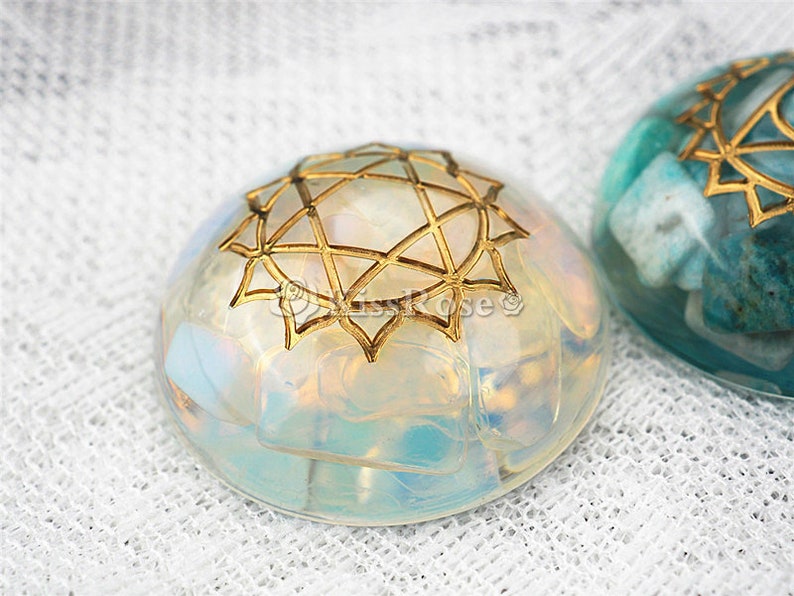 May include: Two round, clear resin ornaments with gold geometric designs. One ornament is filled with iridescent white and blue pieces, the other is filled with blue and green pieces.