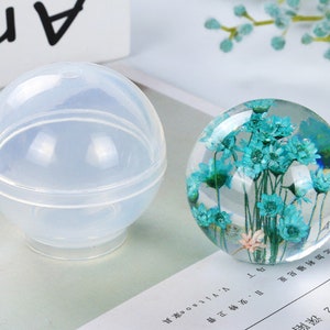 May include: A clear, round silicone mold for resin casting, with a smaller, removable sphere inside.  A finished resin sphere with blue flowers inside is shown next to the mold.