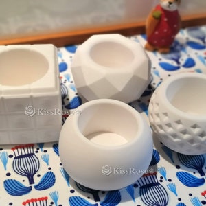 May include: Four white ceramic planters of different shapes and sizes. The planters are on a white and blue patterned surface.
