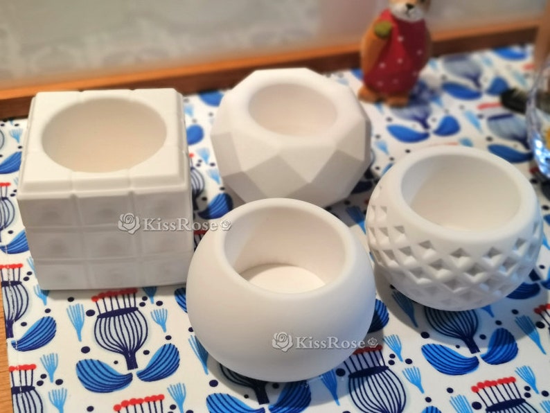May include: Four white ceramic planters of different shapes and sizes. The planters are on a white and blue patterned surface.
