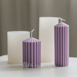 May include: Three candles, two white and one purple, with a ribbed design. The purple candle is taller than the white candles.