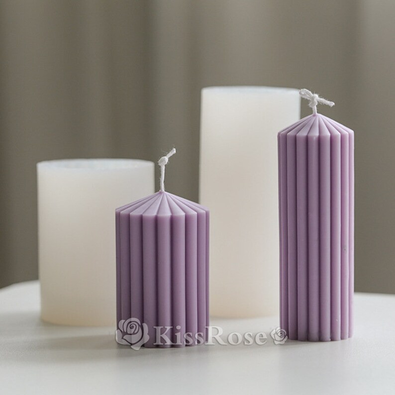 May include: Three candles, two white and one purple, with a ribbed design. The purple candle is taller than the white candles.